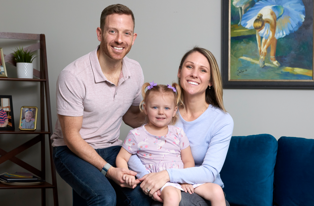 Benjamin Prosser sitting next to his daughter, Lucy, and wife, Erin, on their living room couch